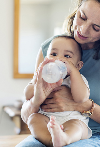 baby drinking milk from bottle on moms lap